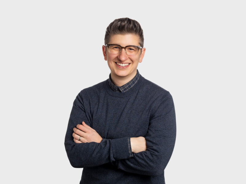 Rebecca Bitterman, a woman with short brown hair wearing a gray pullover and glasses, with her arms folded across her chest.