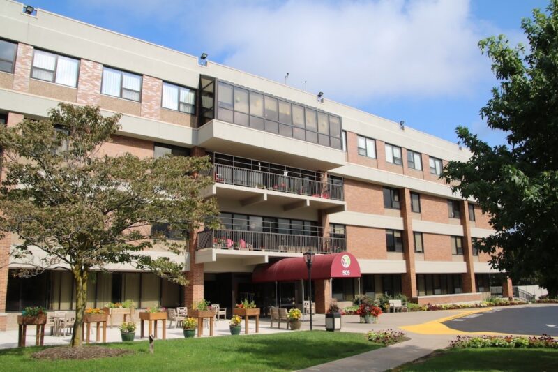 An exterior shot of the main entry for the Episcopal SeniorLife Communities Church Home at 505 Mount Hope Avenue in Rochester, NY. A blue sky in the background shows white clouds.