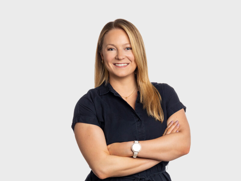 Jennifer Sandora, a woman with long blonde hair, a black short-sleeved blouse, and her arms folded across her chest. She is smiling at the camera.